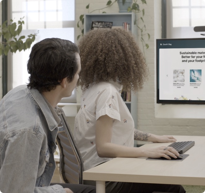 Two teammates collaborating at a desk with a kiosk display
